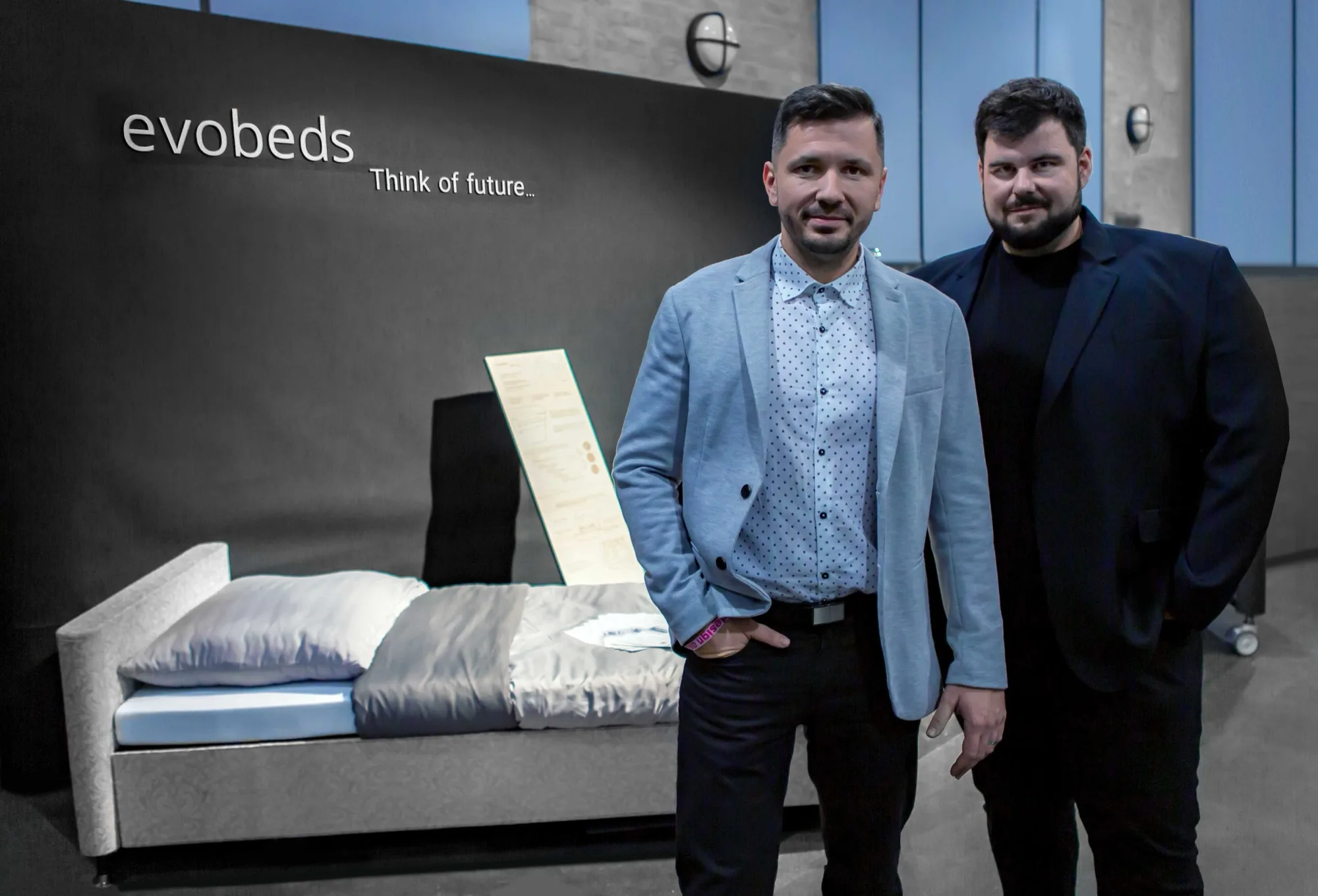 Founders of evobeds by a bed at an exhibition, with the sign evobeds Think of future in the background